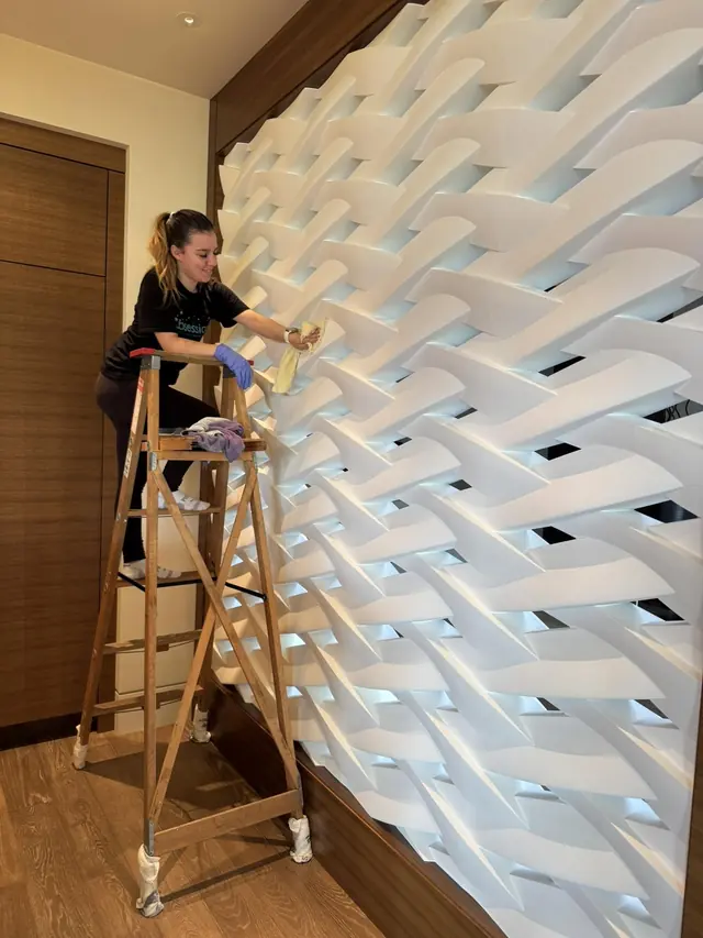Cleaning Technician on a ladder cleaning a sculpted white wall panel
